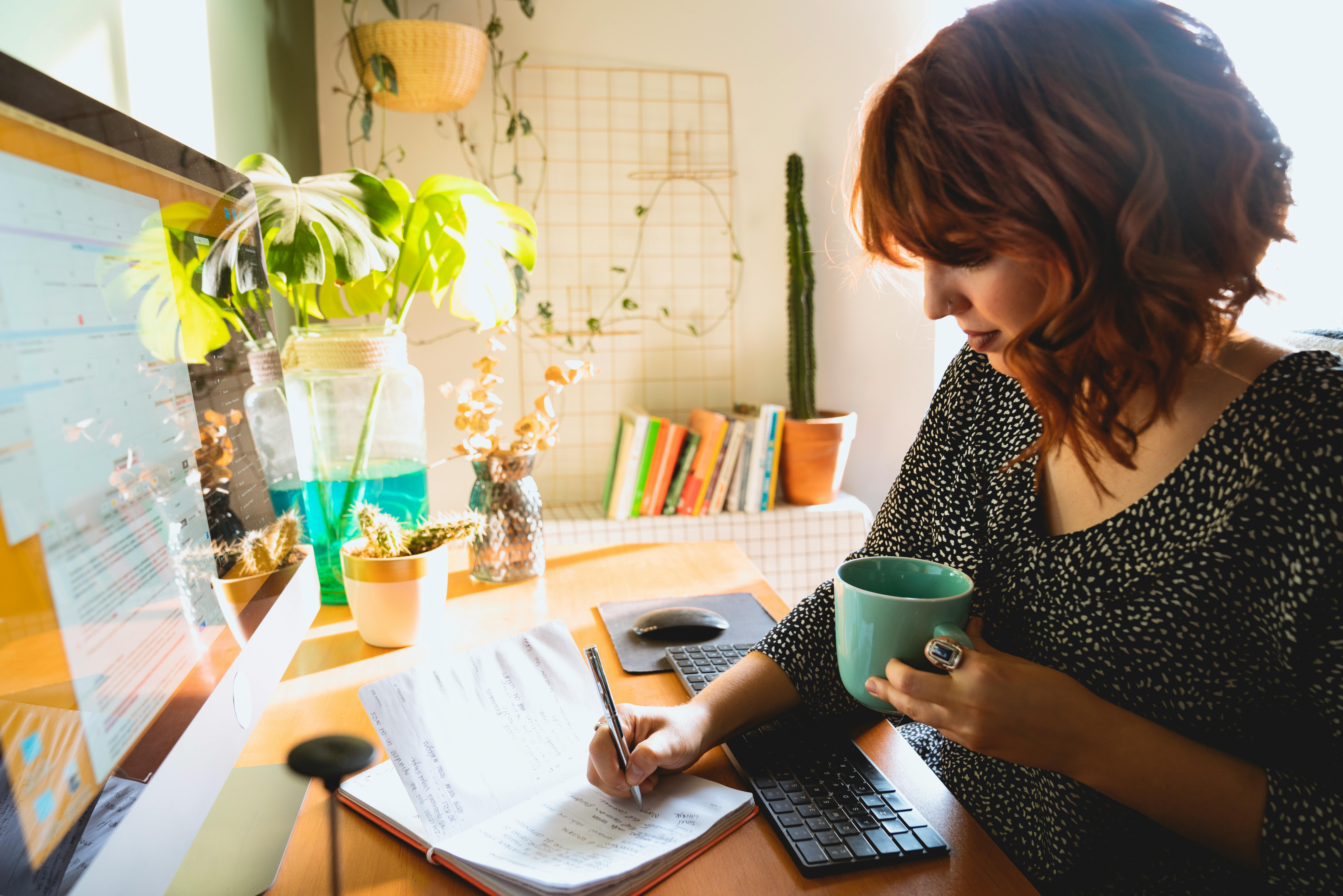 Woman Writing on Her Notebook while Holding a Cup